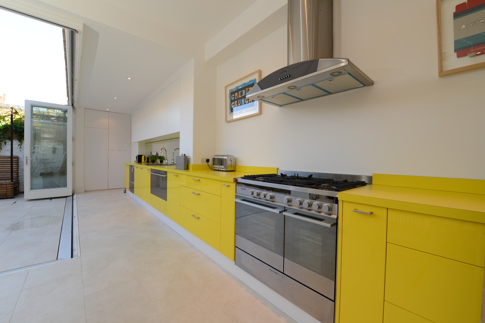 Photo of a contemporary galley kitchen/diner in London with a double-bowl sink, flat-panel cabinets, yellow cabinets, mirror splashback and stainless steel appliances.