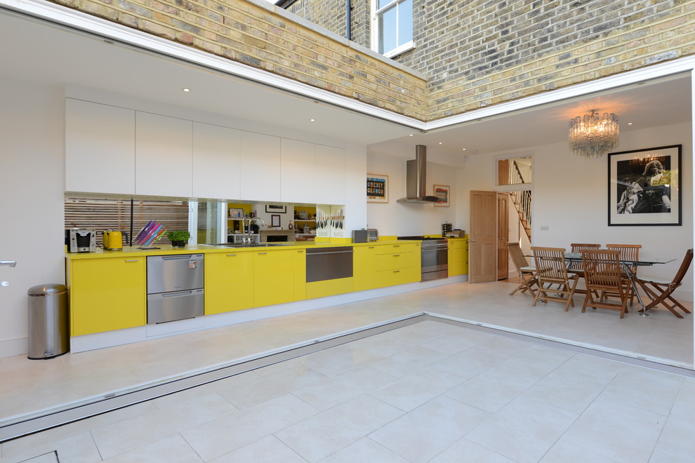 Свежая идея для дизайна: параллельная кухня среднего размера в современном стиле с двойной мойкой, плоскими фасадами, желтыми фасадами, зеркальным фартуком, техникой из нержавеющей стали и обеденным столом - отличное фото интерьера