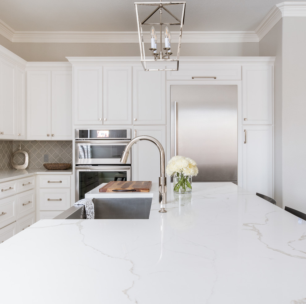Photo of a medium sized classic l-shaped kitchen/diner in Dallas with a submerged sink, shaker cabinets, white cabinets, engineered stone countertops, grey splashback, porcelain splashback, stainless steel appliances, porcelain flooring, an island, white floors and white worktops.