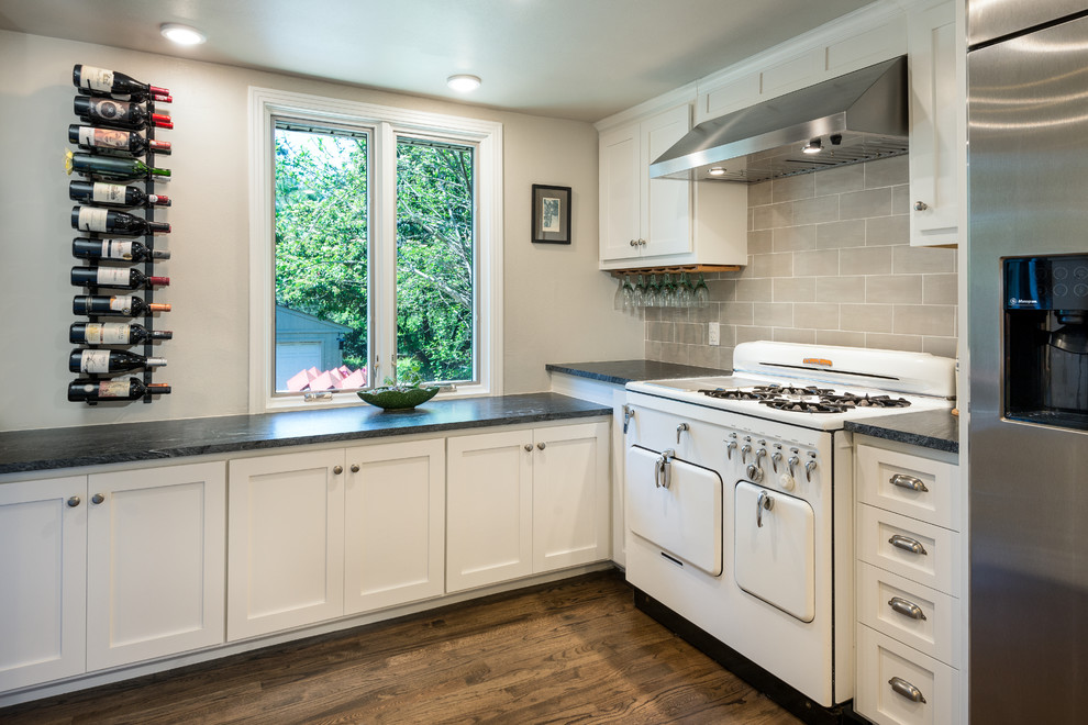 Huge trendy u-shaped dark wood floor and brown floor enclosed kitchen photo in Dallas with an undermount sink, shaker cabinets, white cabinets, soapstone countertops, gray backsplash, stainless steel appliances, black countertops, subway tile backsplash and two islands