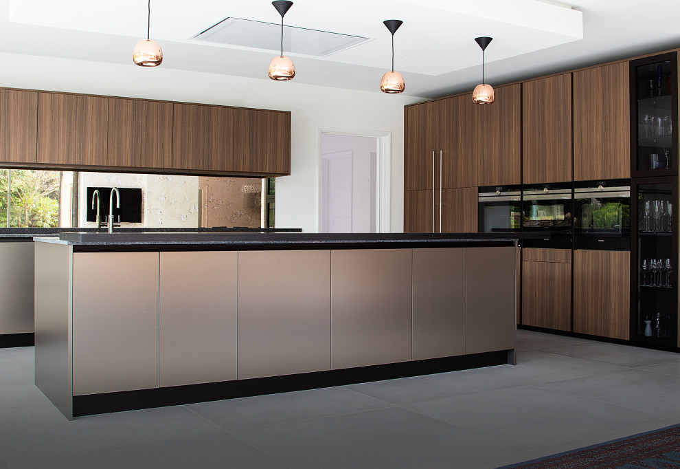 Mittelgroße Moderne Küche mit Granit-Arbeitsplatte, Glasrückwand, schwarzen Elektrogeräten, Kücheninsel und grauem Boden in Sonstige