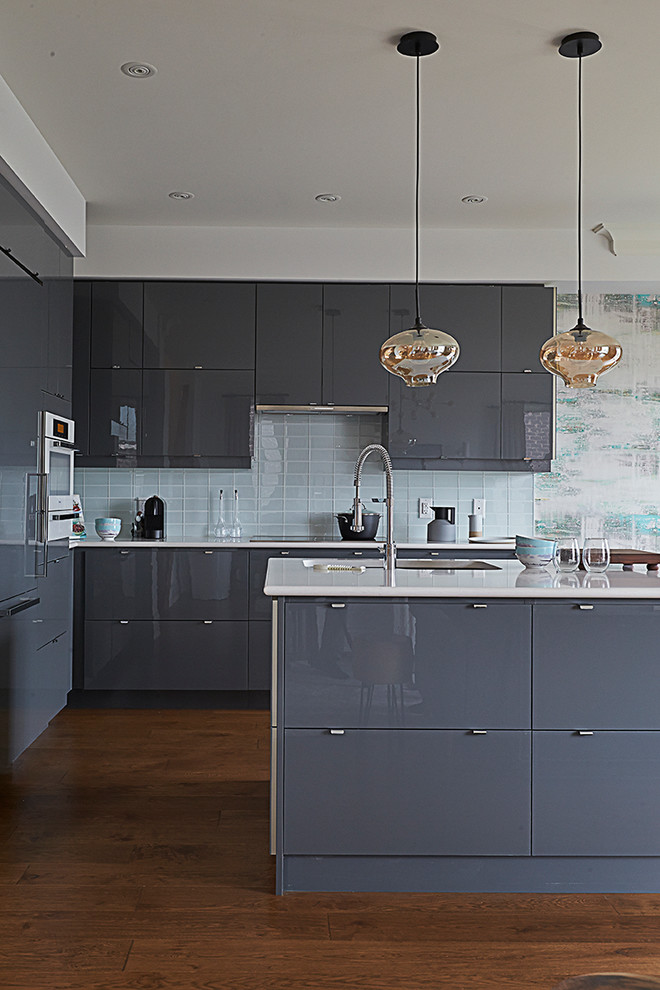 Moderne Küche in L-Form mit Unterbauwaschbecken, flächenbündigen Schrankfronten, grauen Schränken, Küchenrückwand in Blau, Rückwand aus Glasfliesen, dunklem Holzboden und Kücheninsel in Toronto