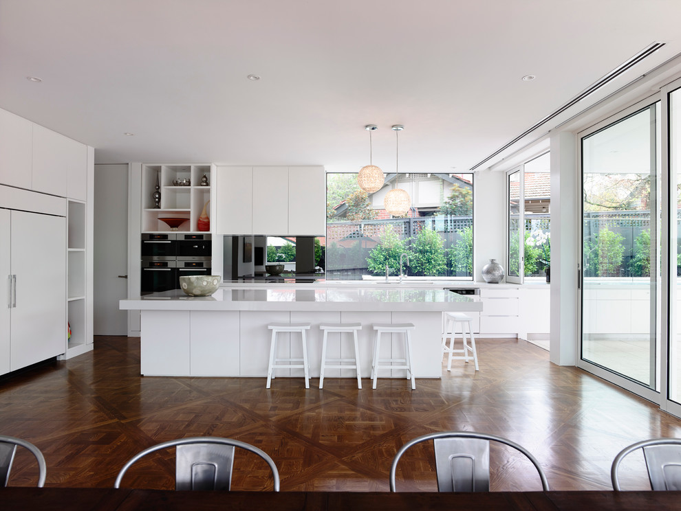Moderne Wohnküche mit flächenbündigen Schrankfronten, weißen Schränken, Elektrogeräten mit Frontblende und Mauersteinen in Melbourne