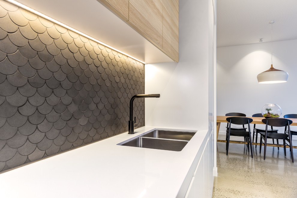 Contemporary galley kitchen pantry in Melbourne with a submerged sink, flat-panel cabinets, light wood cabinets, composite countertops, grey splashback, stone tiled splashback, stainless steel appliances, concrete flooring and an island.