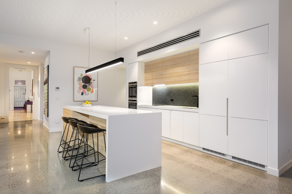 Inspiration for a contemporary galley concrete floor kitchen pantry remodel in Melbourne with an undermount sink, flat-panel cabinets, light wood cabinets, solid surface countertops, gray backsplash, stone tile backsplash, stainless steel appliances and an island