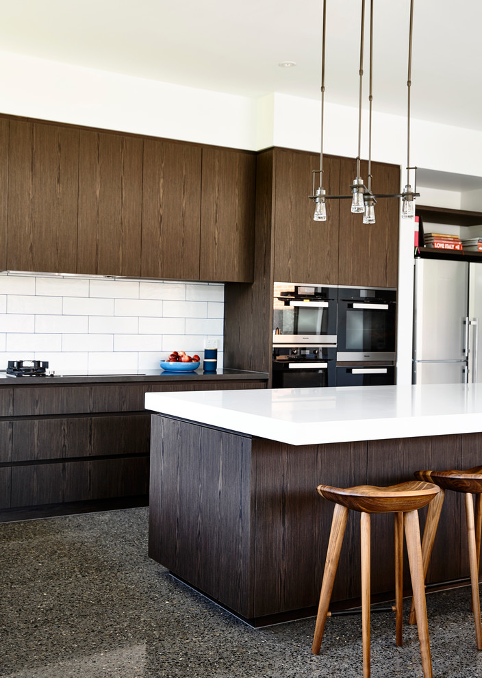 Photo of a large contemporary l-shaped open plan kitchen in Melbourne with a double-bowl sink, flat-panel cabinets, dark wood cabinets, composite countertops, white splashback, ceramic splashback, stainless steel appliances, concrete flooring and an island.