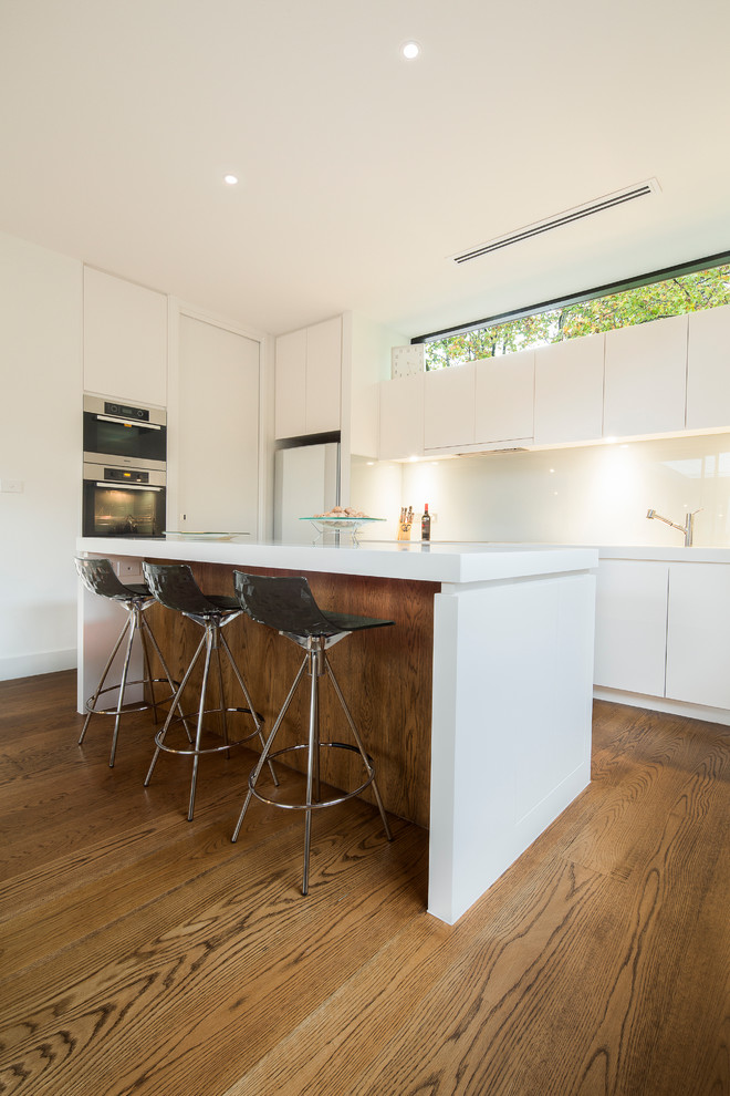 Inspiration for a mid-sized modern galley medium tone wood floor eat-in kitchen remodel in Melbourne with an undermount sink, flat-panel cabinets, white cabinets, quartz countertops, white backsplash, glass sheet backsplash, stainless steel appliances and an island