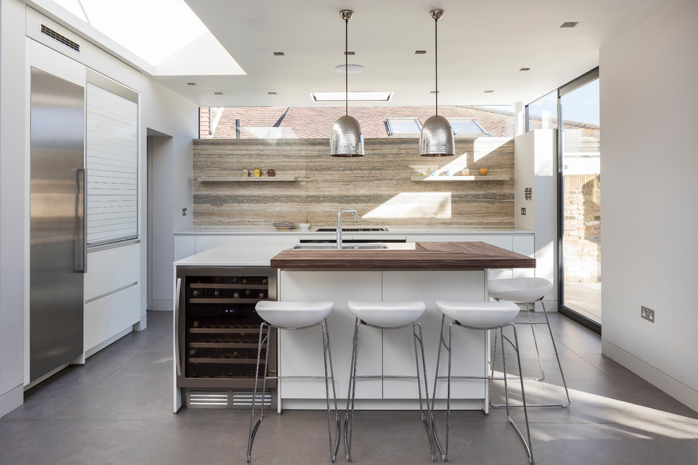 Example of a large trendy gray floor and porcelain tile open concept kitchen design in London with an island, a drop-in sink, white cabinets, quartz countertops, beige backsplash, travertine backsplash, stainless steel appliances, flat-panel cabinets and white countertops