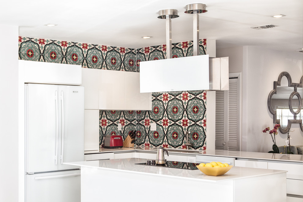 Eat-in kitchen - mid-sized eclectic l-shaped ceramic tile and beige floor eat-in kitchen idea in Miami with an undermount sink, flat-panel cabinets, white cabinets, solid surface countertops, multicolored backsplash, ceramic backsplash, stainless steel appliances and an island