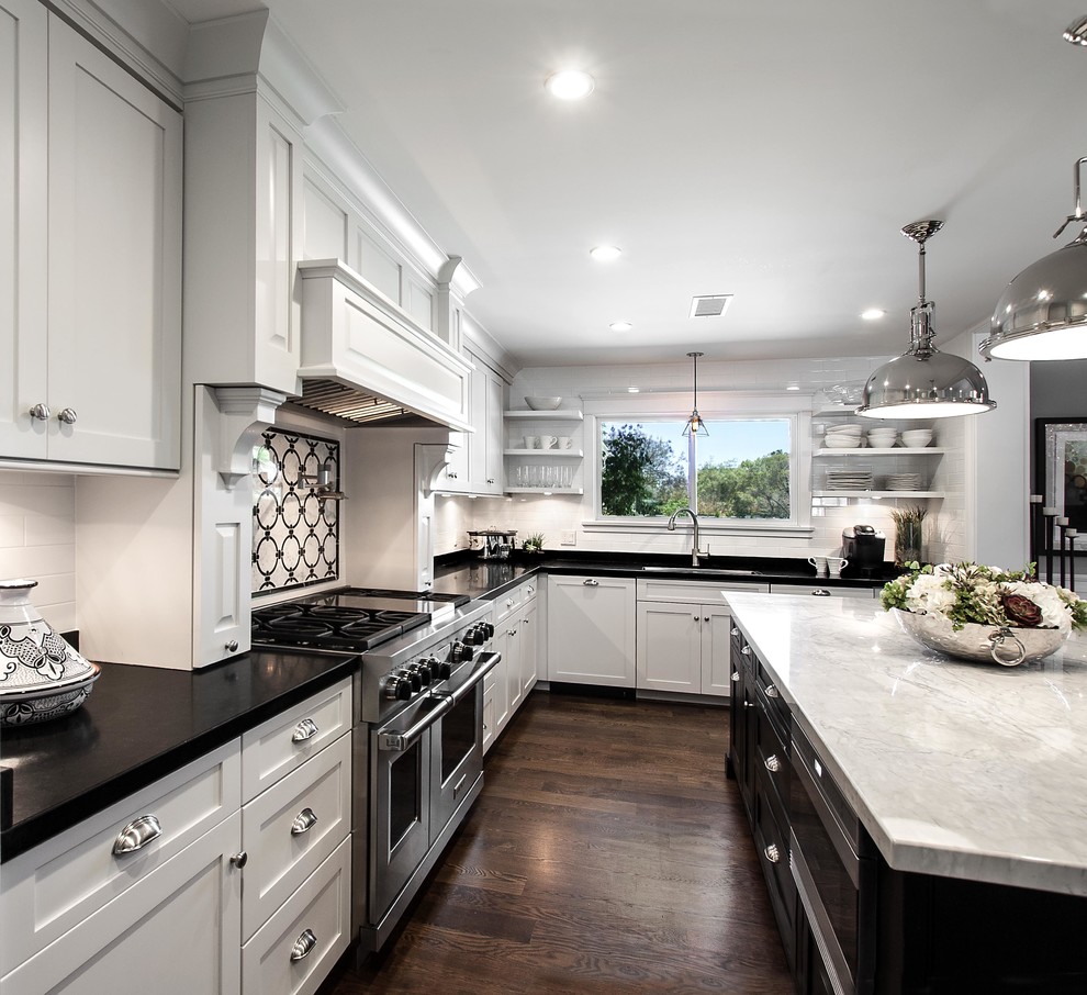 Example of a mid-sized transitional u-shaped medium tone wood floor open concept kitchen design in Los Angeles with an undermount sink, shaker cabinets, white cabinets, marble countertops, white backsplash, ceramic backsplash, stainless steel appliances and an island