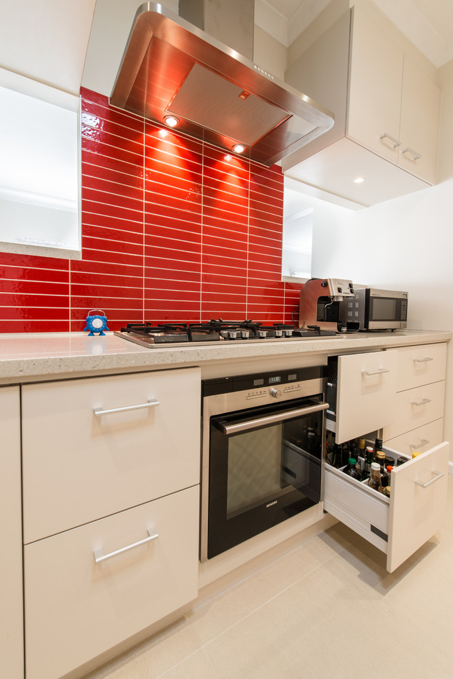 Foto på ett funkis kök, med släta luckor, vita skåp och rött stänkskydd