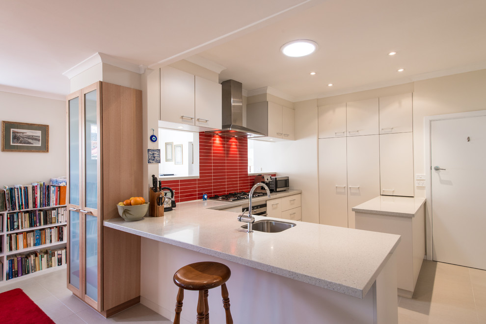 Exempel på ett mellanstort modernt l-kök, med släta luckor, vita skåp, rött stänkskydd, en enkel diskho, stänkskydd i mosaik, rostfria vitvaror, klinkergolv i porslin, en köksö och beiget golv