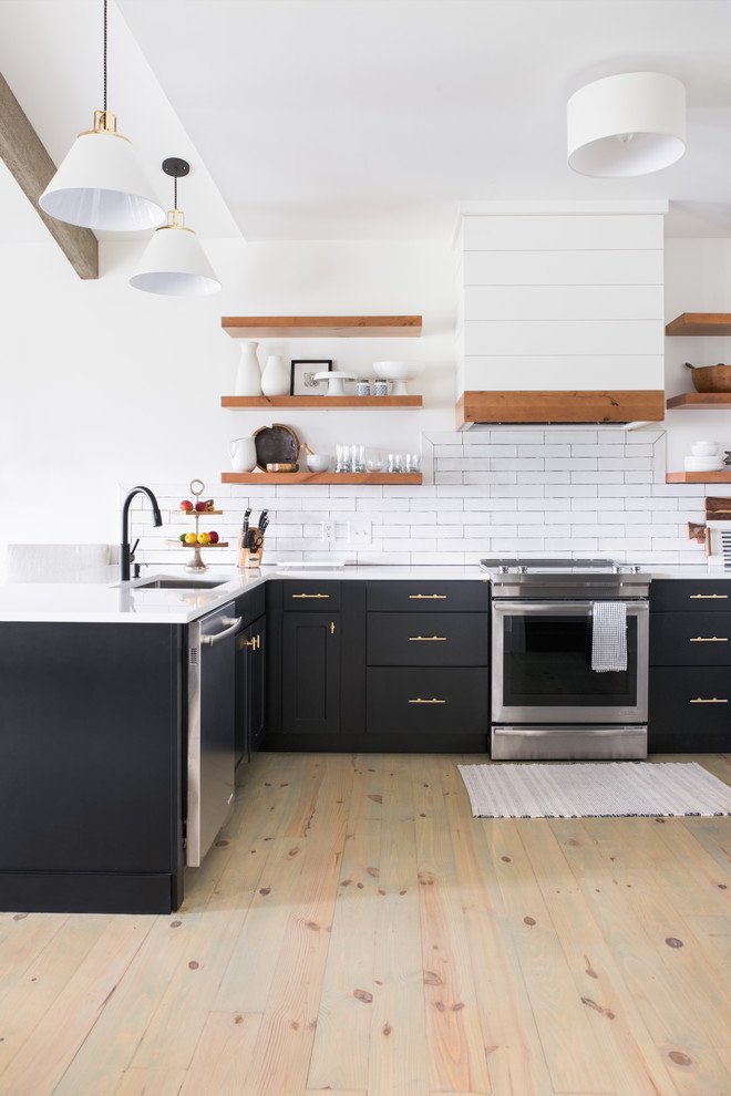 This is an example of a traditional u-shaped kitchen in Charleston with a submerged sink, shaker cabinets, black cabinets, white splashback, metro tiled splashback, stainless steel appliances and light hardwood flooring.