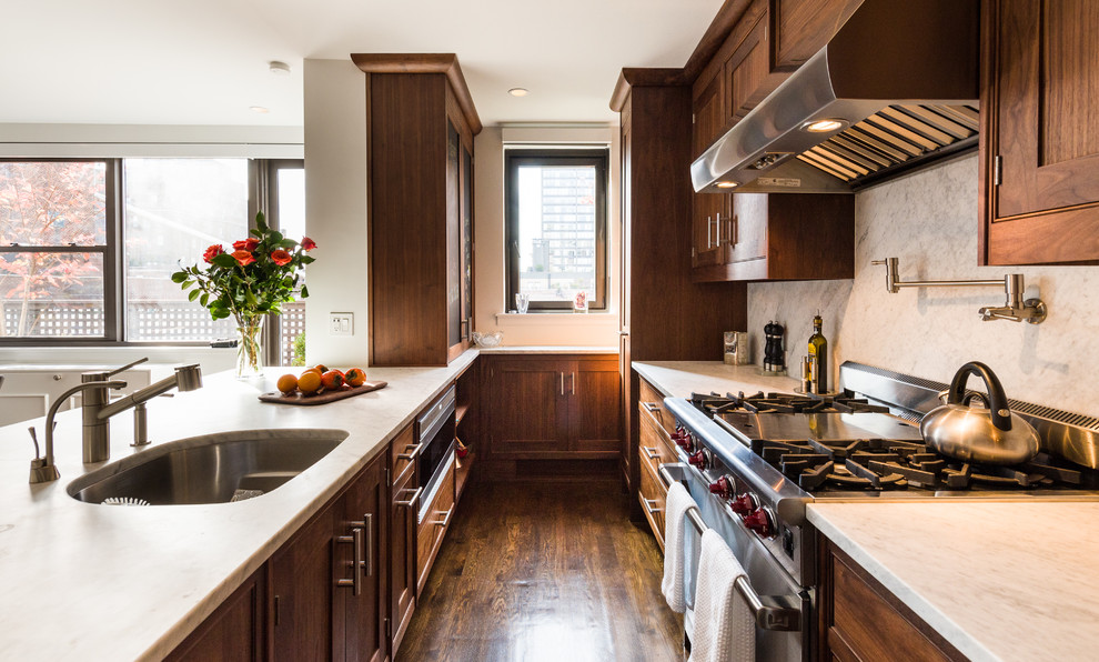 Bild på ett funkis kök, med en undermonterad diskho, luckor med upphöjd panel, skåp i mörkt trä, marmorbänkskiva, vitt stänkskydd, stänkskydd i stenkakel, rostfria vitvaror, mellanmörkt trägolv, en halv köksö och brunt golv