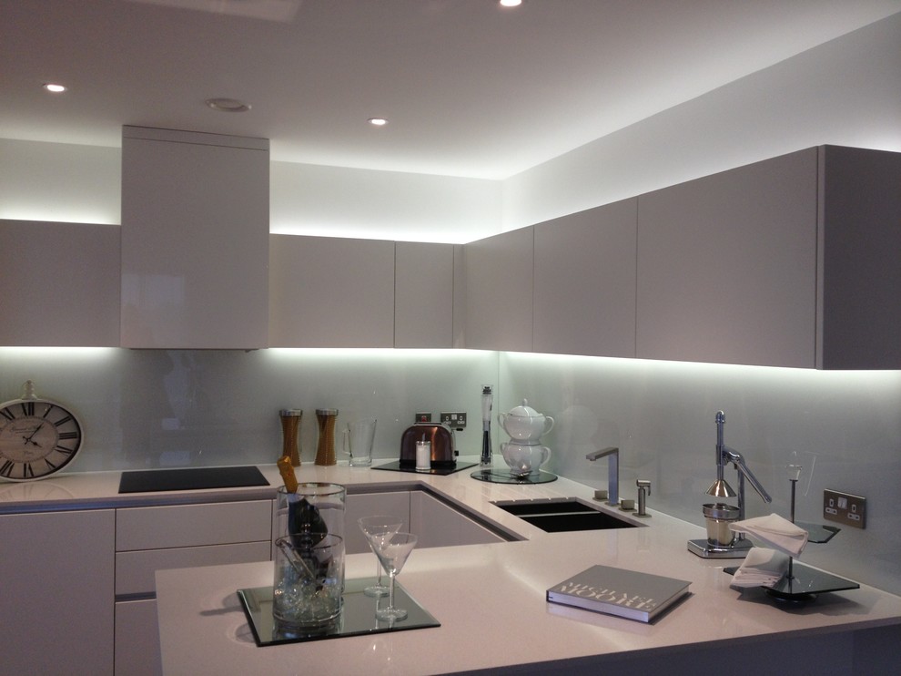 This is an example of a medium sized contemporary u-shaped open plan kitchen in London with a submerged sink, flat-panel cabinets, white cabinets, composite countertops, blue splashback, glass sheet splashback and no island.