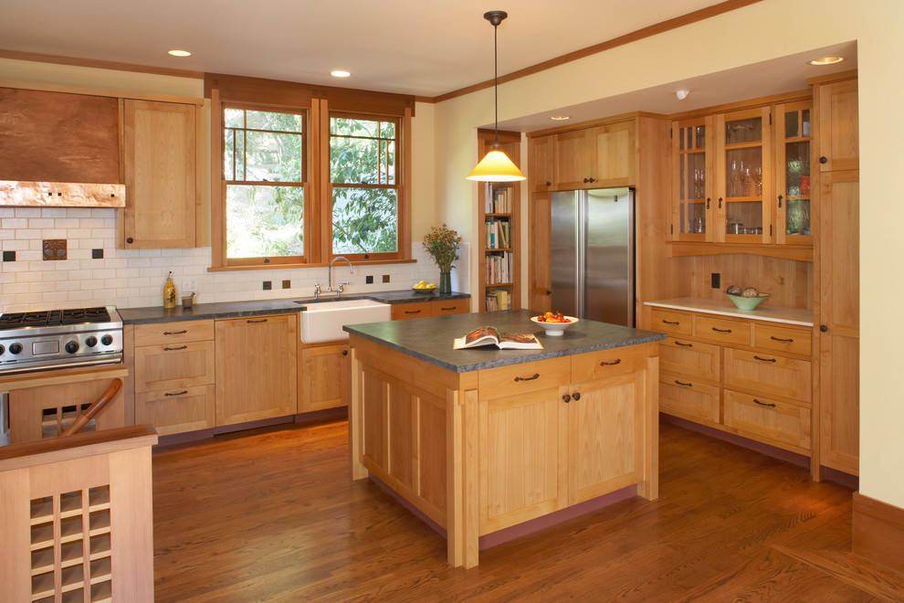 Example of an arts and crafts l-shaped kitchen design in San Francisco with a farmhouse sink, shaker cabinets, medium tone wood cabinets, beige backsplash, subway tile backsplash and stainless steel appliances