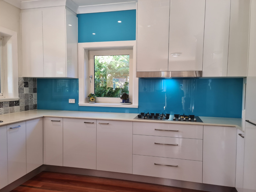This is an example of a medium sized contemporary u-shaped kitchen pantry in Sydney with flat-panel cabinets, white cabinets, blue splashback, glass sheet splashback and no island.