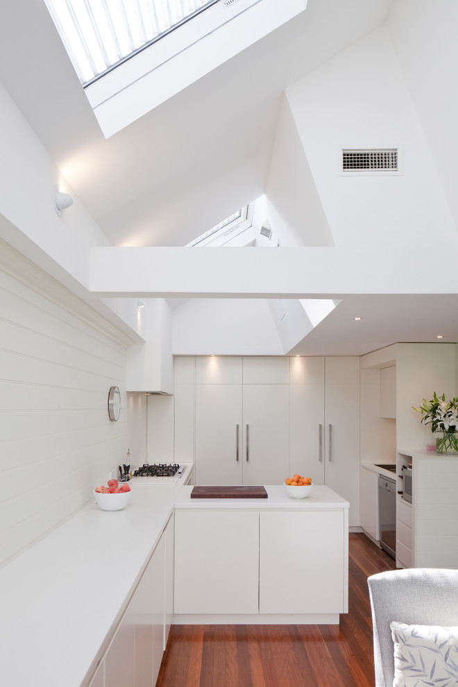 Moderne Küche mit flächenbündigen Schrankfronten, weißen Schränken und braunem Holzboden in Sydney