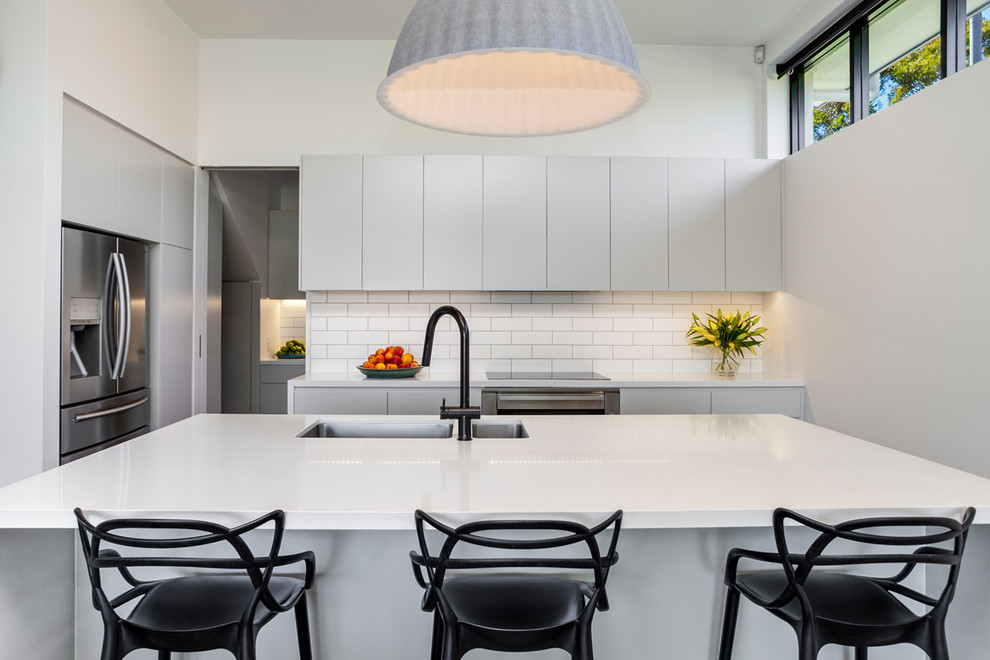 Small contemporary l-shaped kitchen/diner in Sydney with a double-bowl sink, flat-panel cabinets, white cabinets, engineered stone countertops, white splashback, metro tiled splashback, stainless steel appliances and an island.