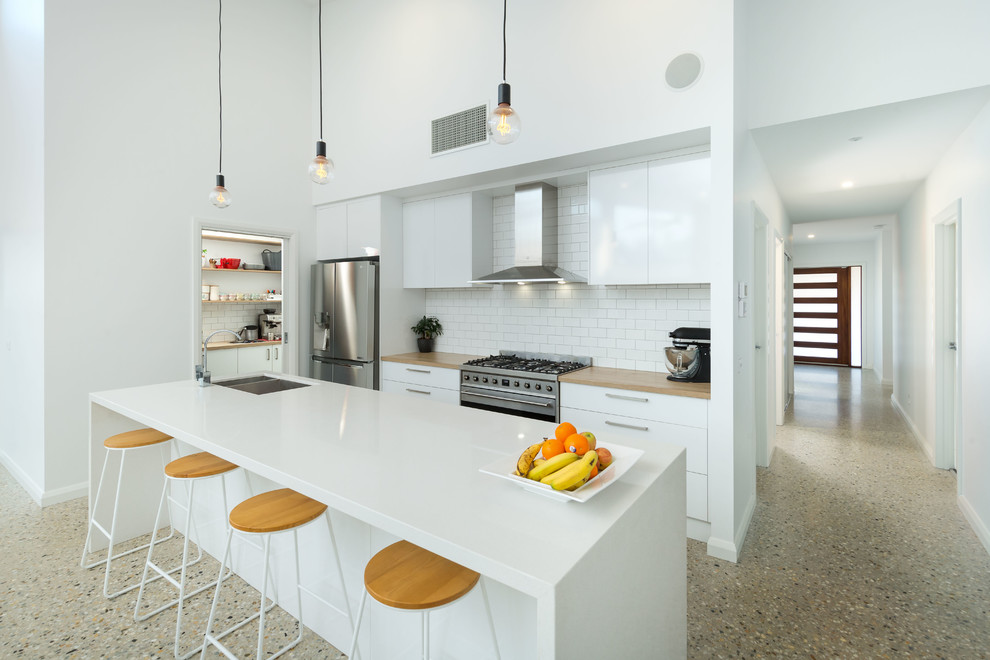 На фото: параллельная кухня в современном стиле с врезной мойкой, плоскими фасадами, белыми фасадами, техникой из нержавеющей стали, островом, бежевым полом и белой столешницей