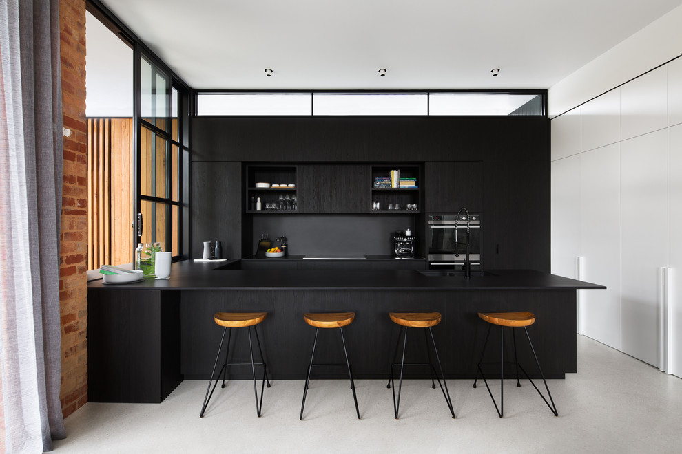 Idee per un cucina con isola centrale con lavello sottopiano, ante lisce, ante nere, elettrodomestici neri, pavimento in cemento, pavimento grigio e top nero