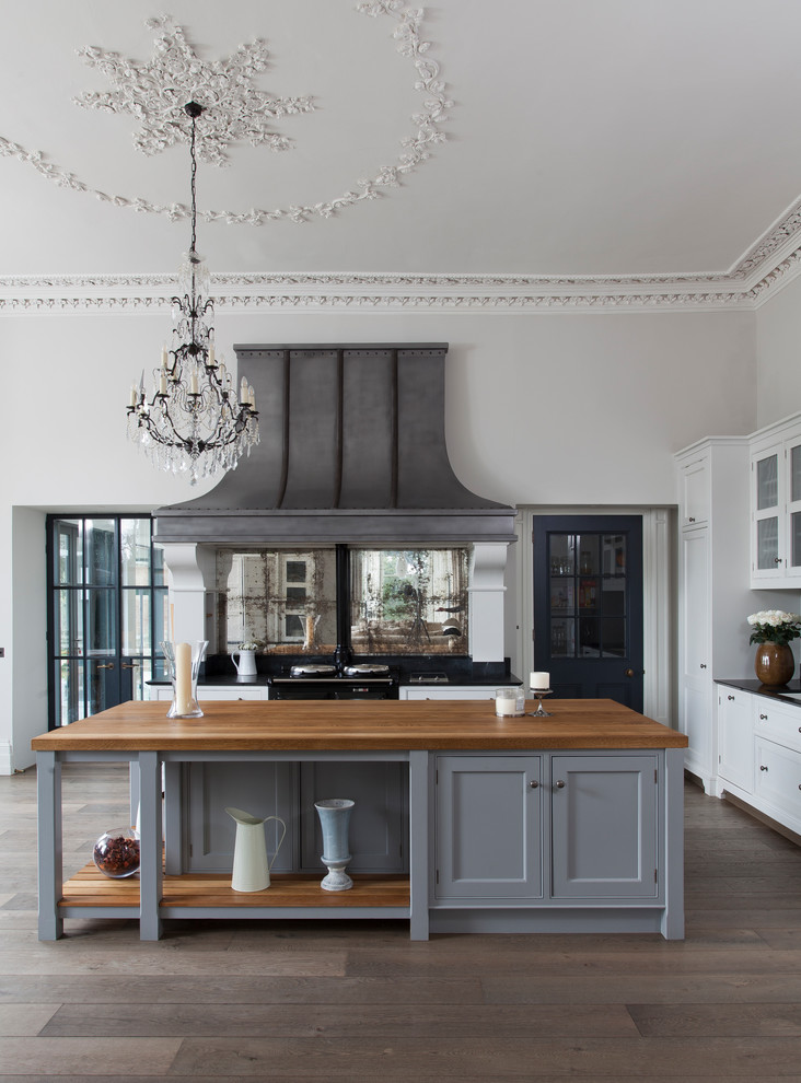 Foto på ett mycket stort vintage kök, med grå skåp, träbänkskiva, stänkskydd med metallisk yta, spegel som stänkskydd, mörkt trägolv, en köksö, luckor med profilerade fronter, svarta vitvaror och brunt golv