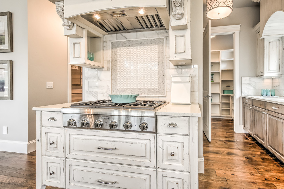 Mid-sized cottage chic u-shaped dark wood floor and brown floor open concept kitchen photo in Boise with a farmhouse sink, raised-panel cabinets, distressed cabinets, quartz countertops, beige backsplash, marble backsplash, stainless steel appliances and an island