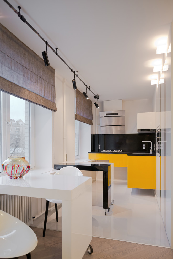 Modern inredning av ett kök, med släta luckor, gula skåp, svart stänkskydd och en halv köksö