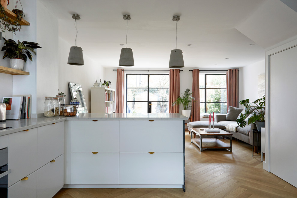 This is an example of a medium sized contemporary l-shaped open plan kitchen in London with a built-in sink, flat-panel cabinets, white cabinets, quartz worktops, stone slab splashback, stainless steel appliances, light hardwood flooring, a breakfast bar and grey worktops.
