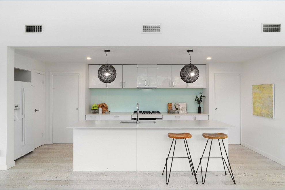 Modern inredning av ett mellanstort kök, med vita skåp, bänkskiva i kvarts, vitt stänkskydd, glaspanel som stänkskydd, laminatgolv, en köksö, vitt golv och en undermonterad diskho