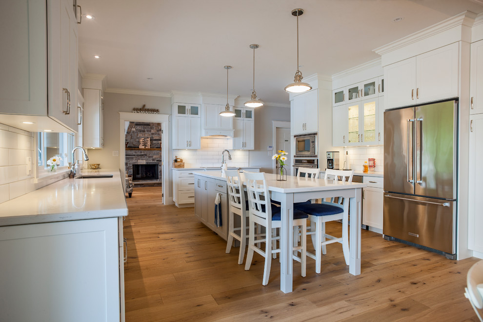Example of a large cottage u-shaped light wood floor and brown floor eat-in kitchen design in Toronto with a single-bowl sink, shaker cabinets, white cabinets, marble countertops, white backsplash, subway tile backsplash, stainless steel appliances and an island