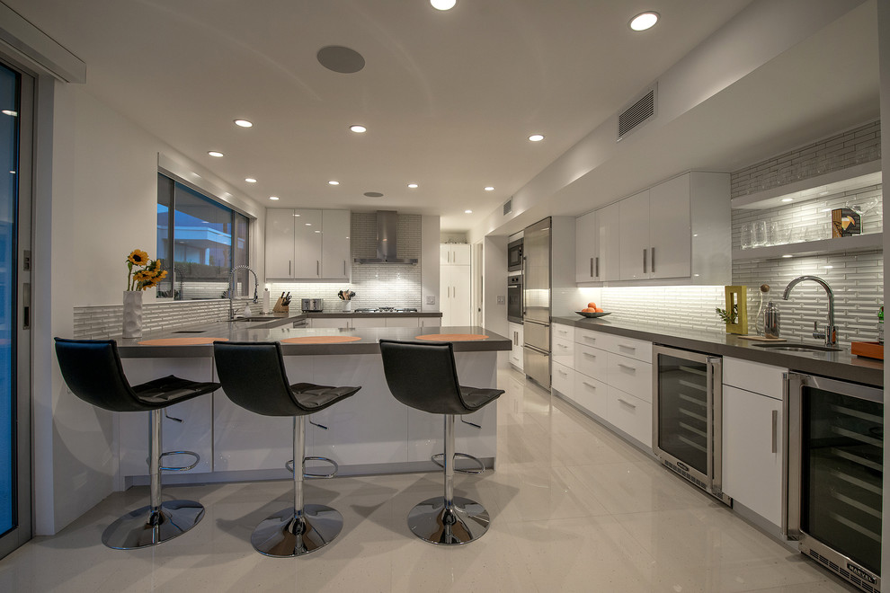 Modern inredning av ett kök, med en enkel diskho, släta luckor, vita skåp, bänkskiva i kvartsit, vitt stänkskydd, stänkskydd i tunnelbanekakel, rostfria vitvaror, klinkergolv i porslin och en halv köksö