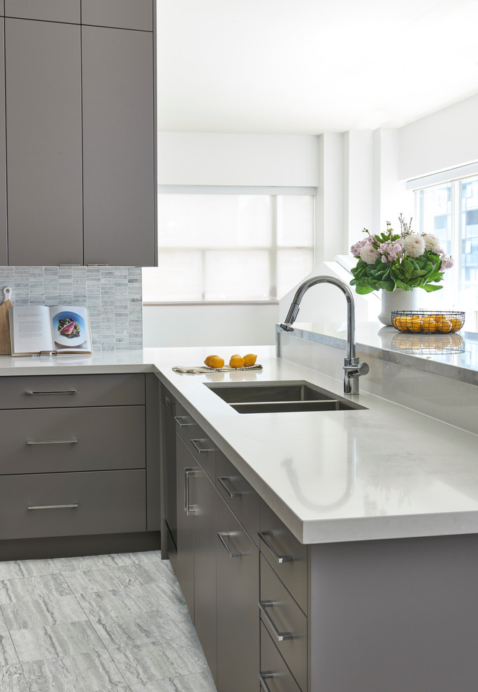 Modern inredning av ett mellanstort kök, med en undermonterad diskho, släta luckor, grå skåp, bänkskiva i kvarts, grått stänkskydd, stänkskydd i stenkakel, rostfria vitvaror, klinkergolv i porslin och en halv köksö