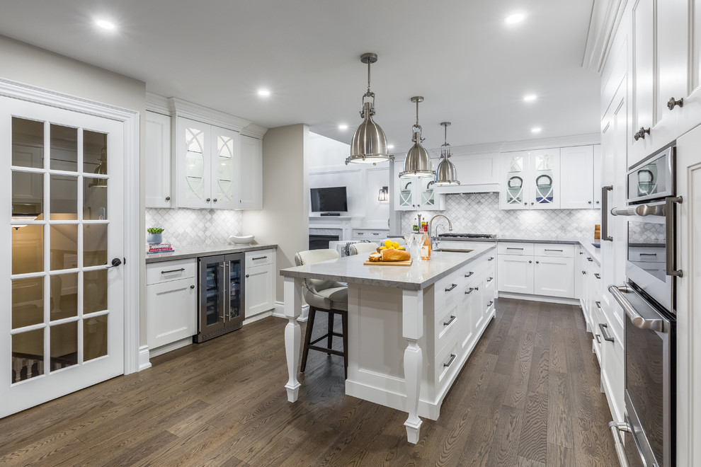 Medium sized traditional u-shaped enclosed kitchen in Toronto with a submerged sink, recessed-panel cabinets, white cabinets, engineered stone countertops, grey splashback, marble splashback, stainless steel appliances, dark hardwood flooring, an island and brown floors.