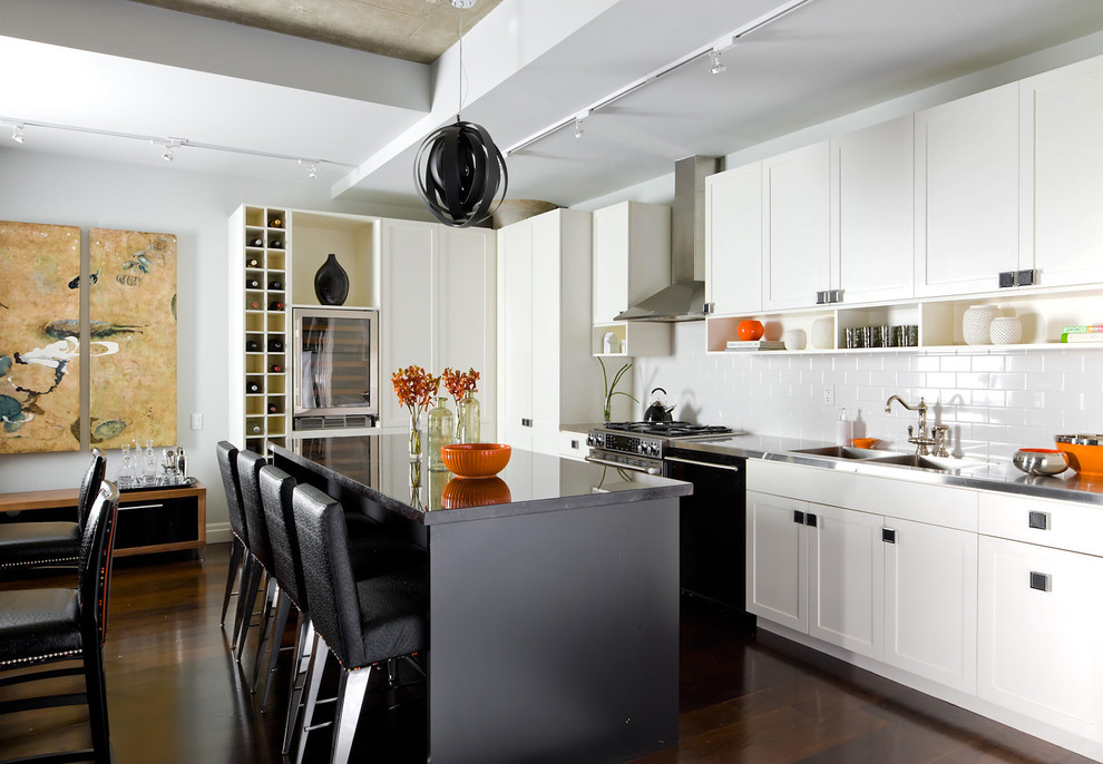 トロントにある高級な中くらいなコンテンポラリースタイルのおしゃれなキッチン (サブウェイタイルのキッチンパネル、シェーカースタイル扉のキャビネット、白いキャビネット、白いキッチンパネル、ダブルシンク、ステンレスカウンター、パネルと同色の調理設備、濃色無垢フローリング、茶色い床) の写真