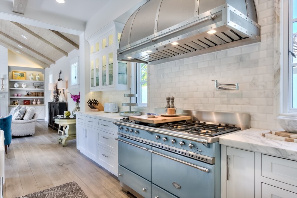 Inspiration for a large farmhouse l-shaped light wood floor open concept kitchen remodel in Orange County with a farmhouse sink, recessed-panel cabinets, white cabinets, marble countertops, white backsplash, subway tile backsplash, stainless steel appliances and an island