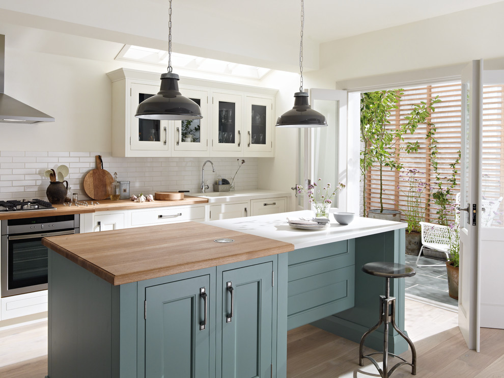 Design ideas for a traditional kitchen in London with recessed-panel cabinets, white cabinets, white splashback, metro tiled splashback, stainless steel appliances, light hardwood flooring and an island.