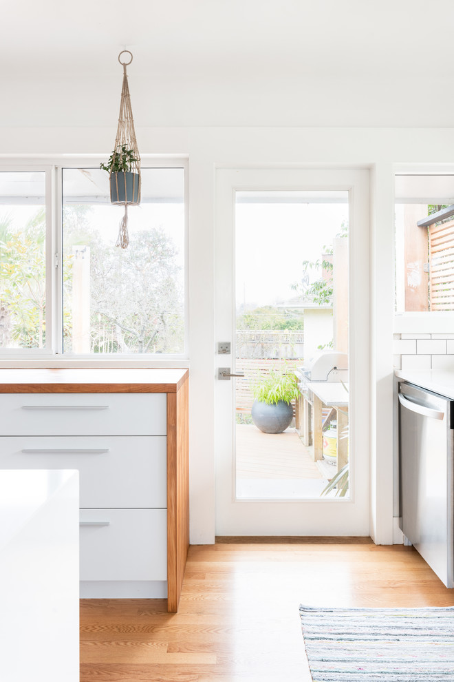 Foto på ett litet skandinaviskt flerfärgad kök, med en undermonterad diskho, släta luckor, vita skåp, träbänkskiva, vitt stänkskydd, stänkskydd i porslinskakel, rostfria vitvaror, mellanmörkt trägolv och brunt golv