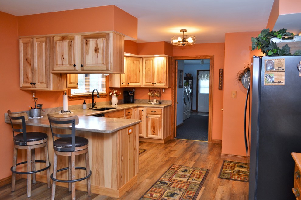 Rustik inredning av ett mellanstort brun brunt kök, med en undermonterad diskho, luckor med upphöjd panel, skåp i ljust trä, bänkskiva i koppar, rostfria vitvaror, laminatgolv, en halv köksö och brunt golv