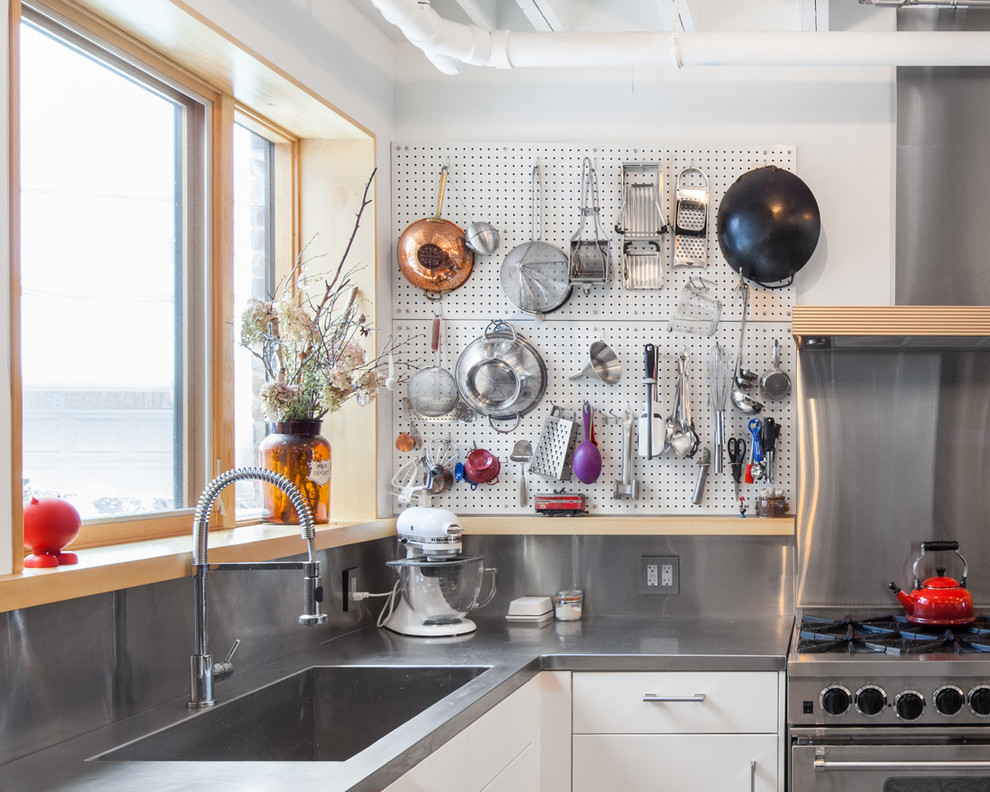 На фото: угловая кухня в стиле лофт с обеденным столом, столешницей из нержавеющей стали и фартуком цвета металлик без острова