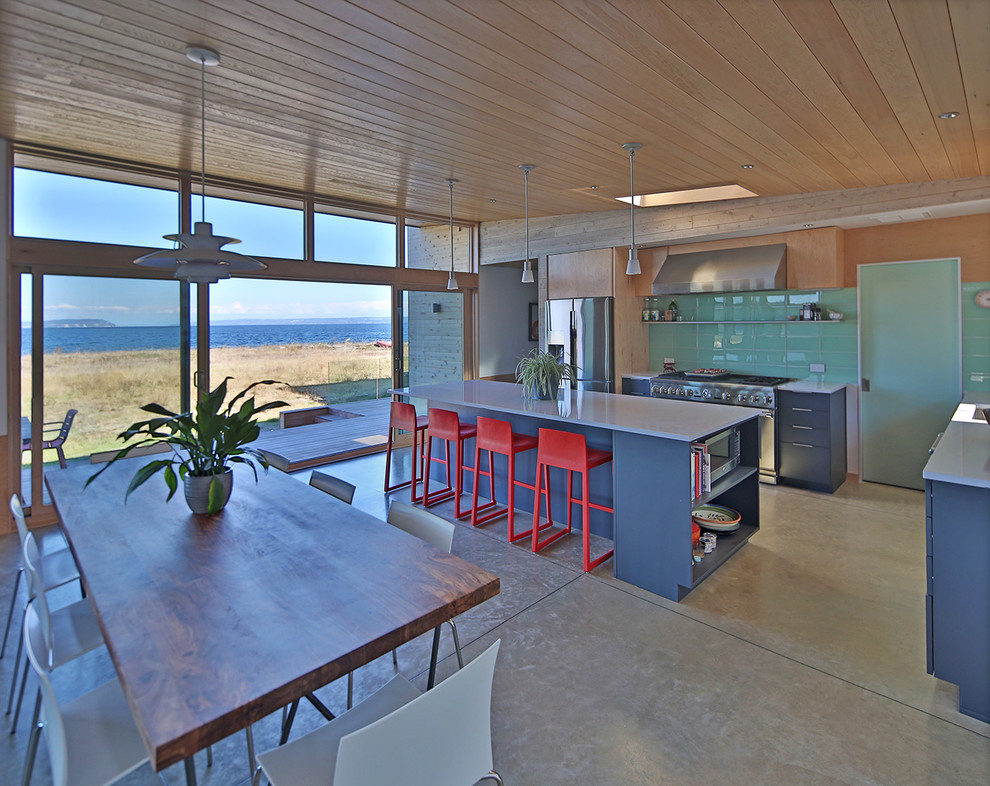 Medium sized modern l-shaped open plan kitchen in Seattle with a submerged sink, flat-panel cabinets, blue cabinets, engineered stone countertops, green splashback, glass tiled splashback, stainless steel appliances, concrete flooring, an island, grey floors and white worktops.