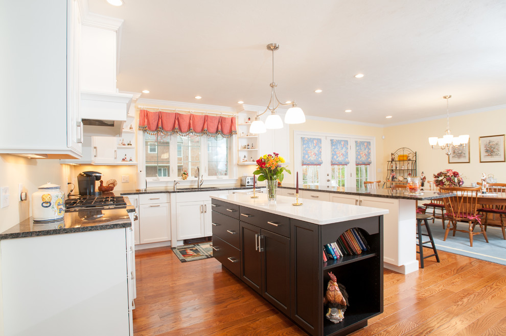Lantlig inredning av ett mellanstort kök, med en undermonterad diskho, skåp i shakerstil, vita skåp, granitbänkskiva, rostfria vitvaror, mellanmörkt trägolv, en köksö och brunt golv