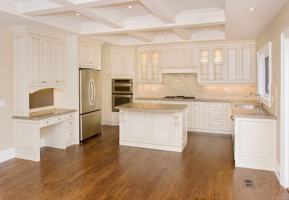Inredning av ett klassiskt mellanstort kök, med en dubbel diskho, luckor med upphöjd panel, vita skåp, granitbänkskiva, beige stänkskydd, stänkskydd i marmor, rostfria vitvaror, mellanmörkt trägolv och en köksö