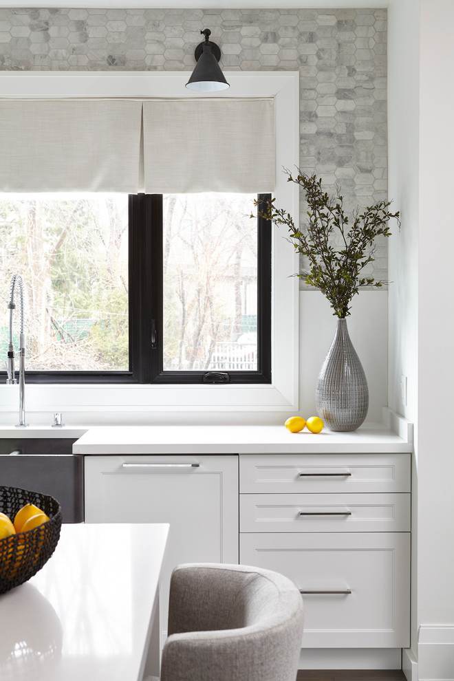 This is an example of a large traditional u-shaped open plan kitchen in Toronto with a belfast sink, shaker cabinets, white cabinets, quartz worktops, grey splashback, stone tiled splashback, stainless steel appliances, medium hardwood flooring, an island, brown floors and white worktops.