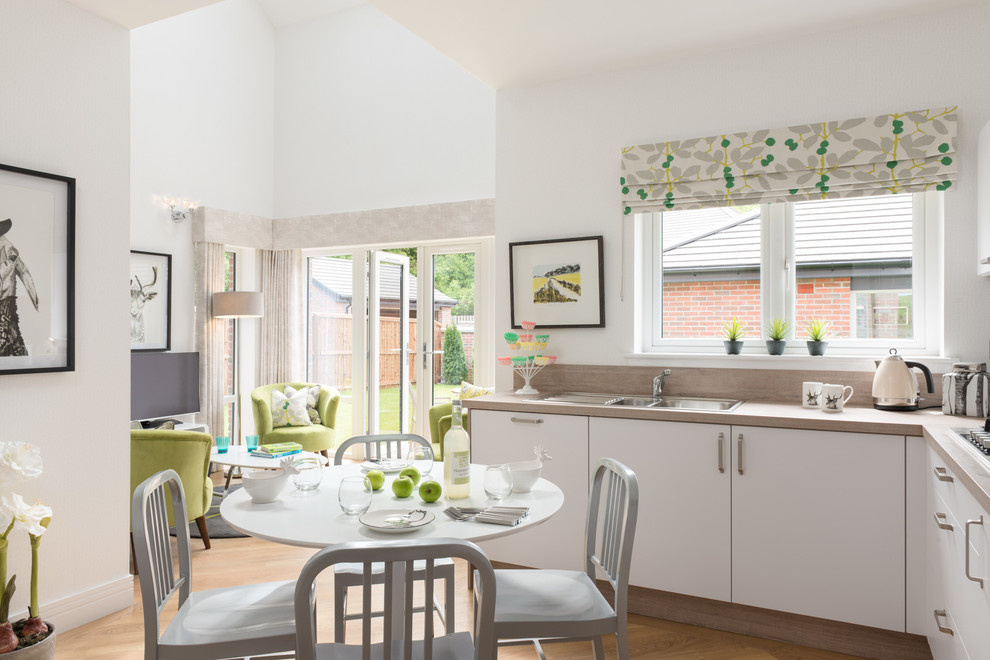 This is an example of a traditional l-shaped open plan kitchen in London with a double-bowl sink, flat-panel cabinets, white cabinets, light hardwood flooring and no island.