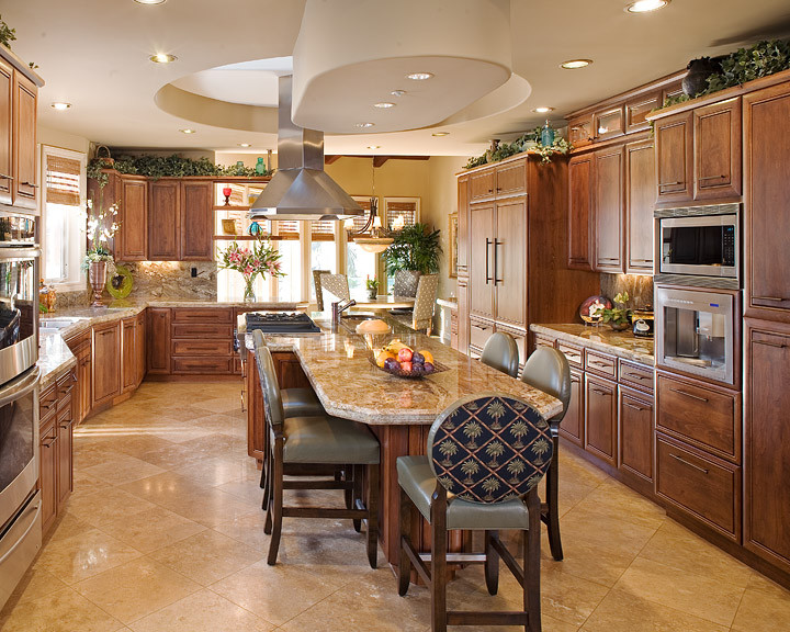 Eat-in kitchen - large tropical u-shaped travertine floor and brown floor eat-in kitchen idea in San Diego with an undermount sink, raised-panel cabinets, dark wood cabinets, granite countertops, brown backsplash, stone slab backsplash, paneled appliances and an island