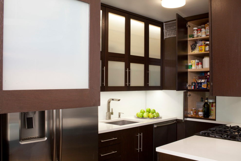 Enclosed kitchen - small contemporary l-shaped enclosed kitchen idea in New York with an undermount sink, glass-front cabinets, brown cabinets, white backsplash, stainless steel appliances and no island
