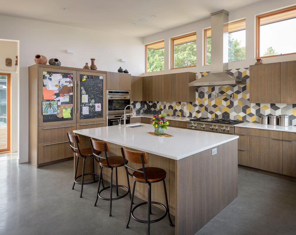 Moderne Küche in L-Form mit Unterbauwaschbecken, flächenbündigen Schrankfronten, hellen Holzschränken, bunter Rückwand, Küchengeräten aus Edelstahl, Betonboden, Kücheninsel, grauem Boden und weißer Arbeitsplatte in Seattle