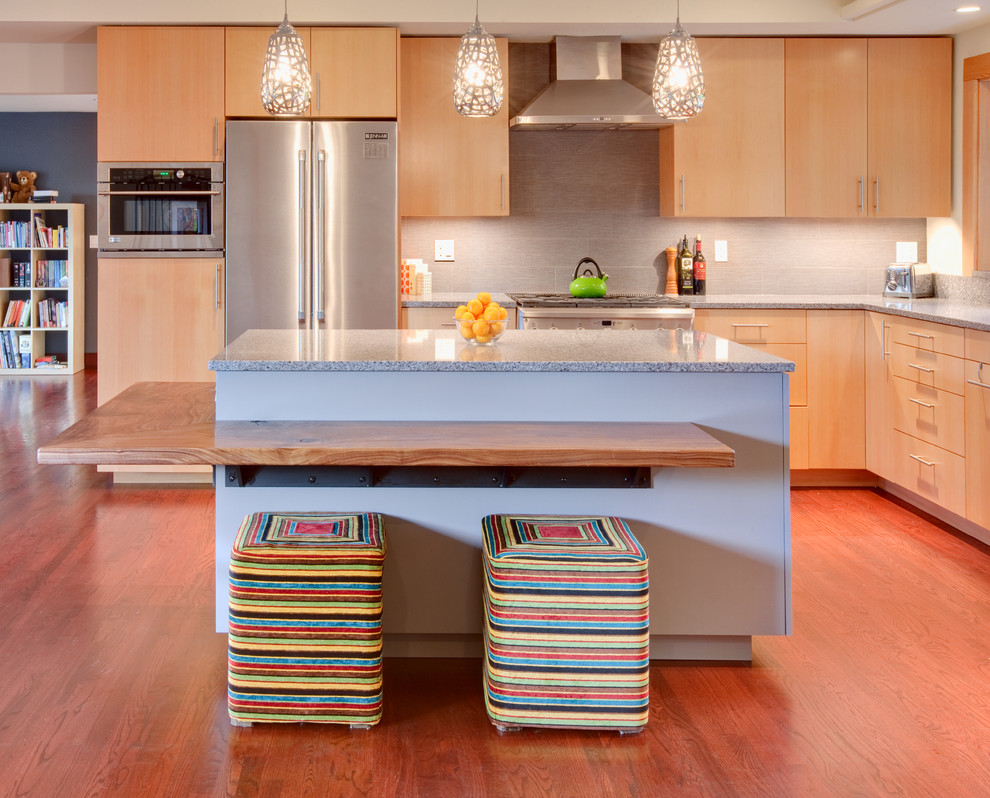 На фото: кухня-гостиная в стиле модернизм с плоскими фасадами, светлыми деревянными фасадами, серым фартуком, техникой из нержавеющей стали и барной стойкой