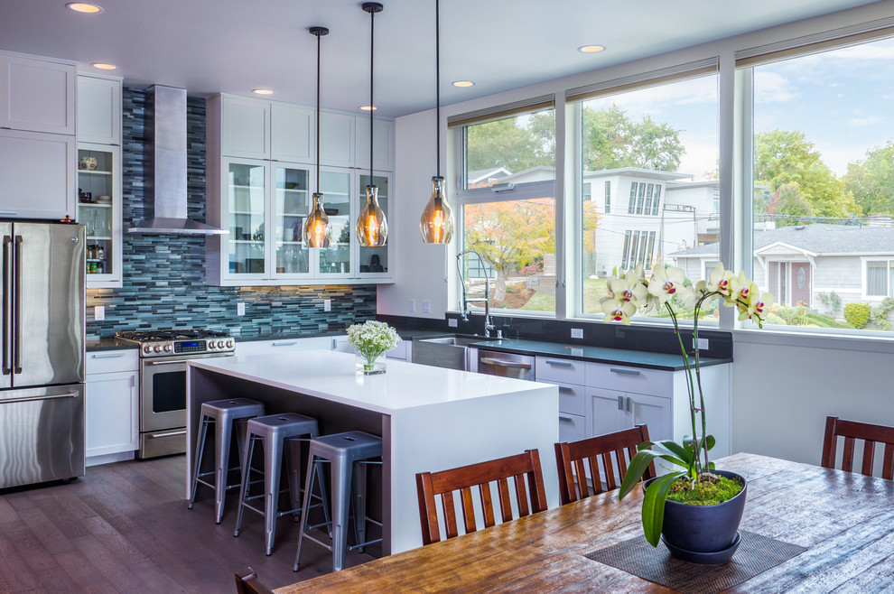 Inspiration for a contemporary l-shaped open plan kitchen in Seattle with glass-front cabinets, white cabinets, blue splashback, an island, a belfast sink, mosaic tiled splashback, stainless steel appliances and medium hardwood flooring.